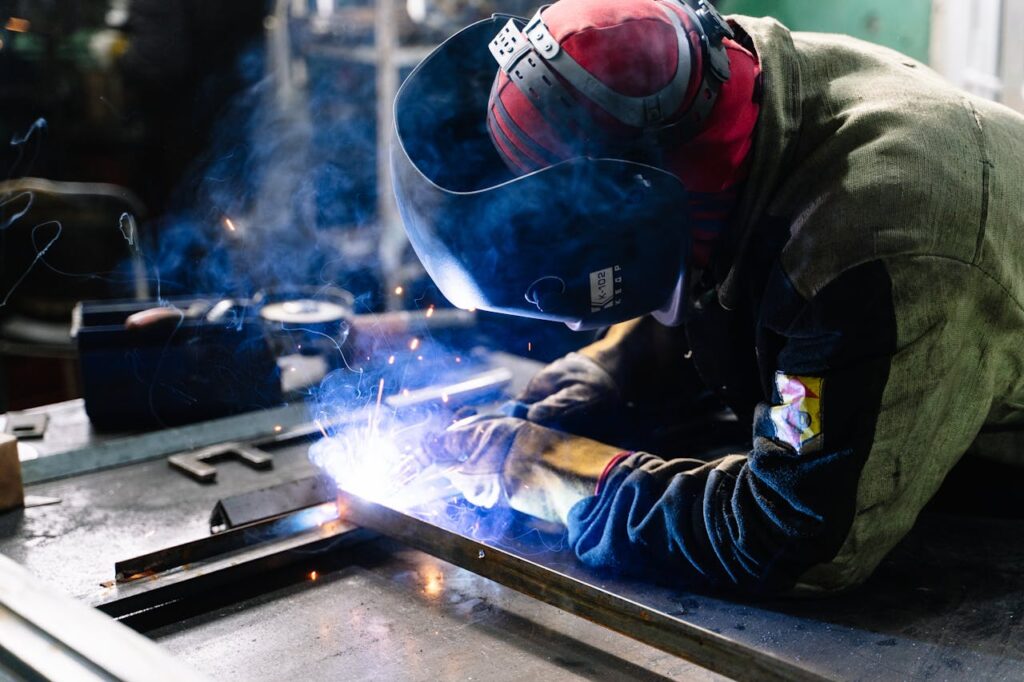 pexels-photo-2381463 A welder works on metal fabrication indoors, creating bright sparks and smoke.
